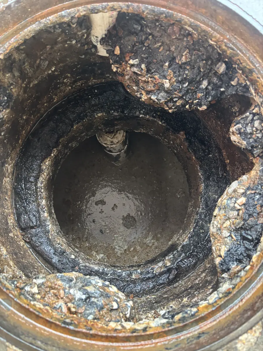 Crumbling concrete riser around the opening of an in-ground grease trap, seen from above with the lid off