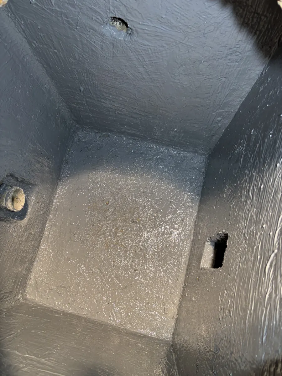 Emptied grease trap after repair, its walls and floor covered in a textured gray coating