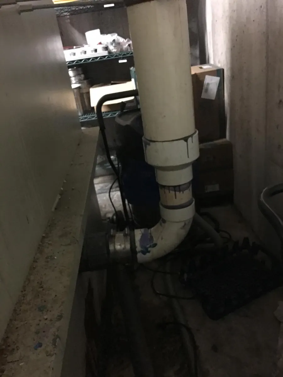 Grease trap unit installed indoors, with a white drain pipe bending into its side