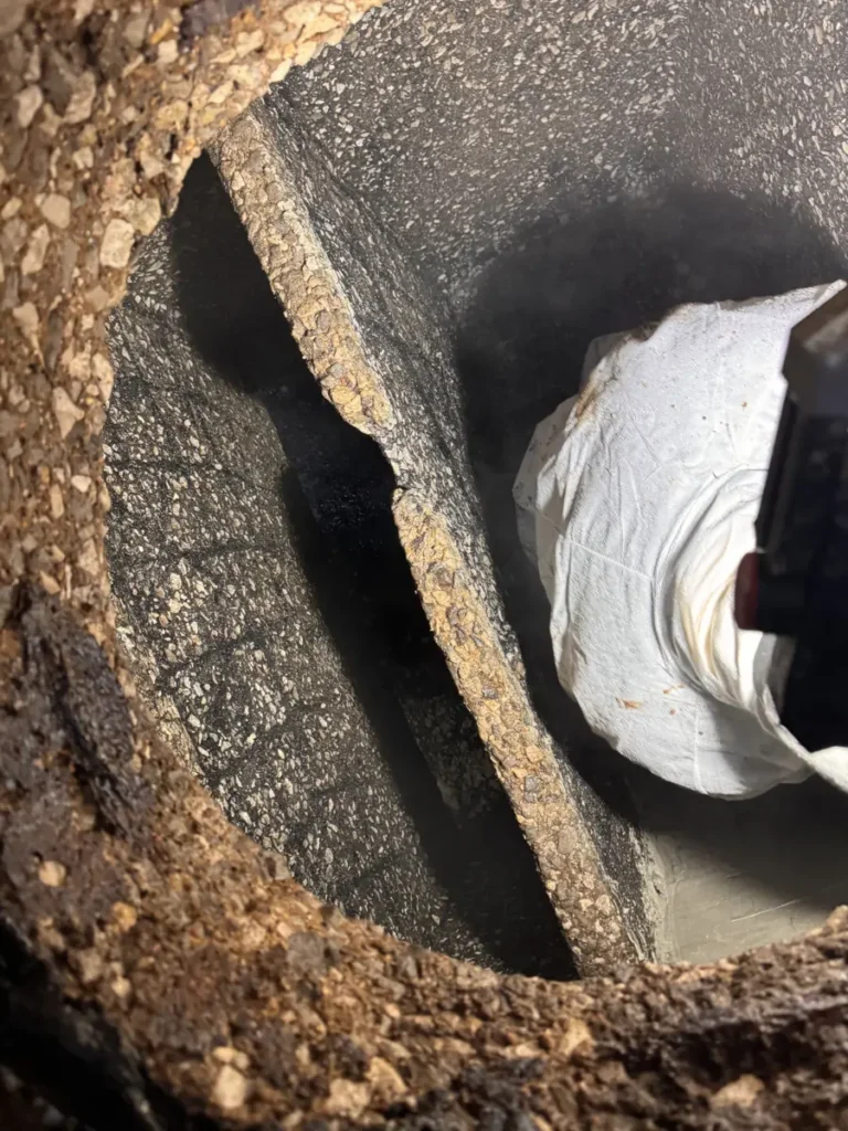 Worker in a protective suit inside an emptied concrete grease trap whose walls and baffle wall are worn down to the stones