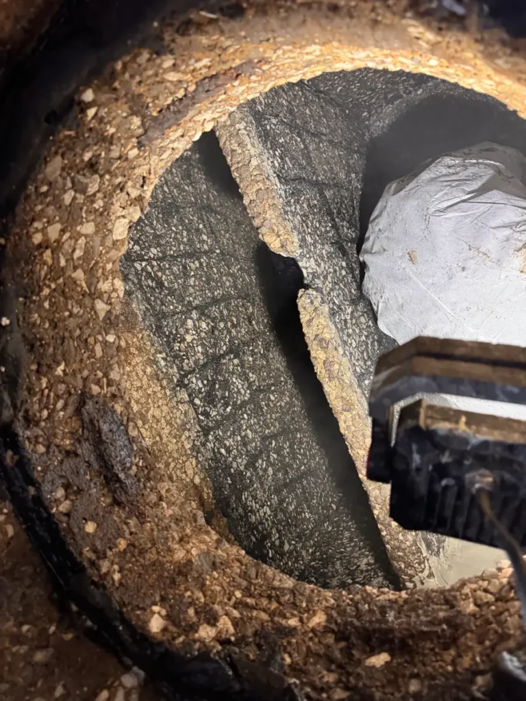 Emptied concrete grease trap seen through the opening, its baffle wall and walls worn down to the stones